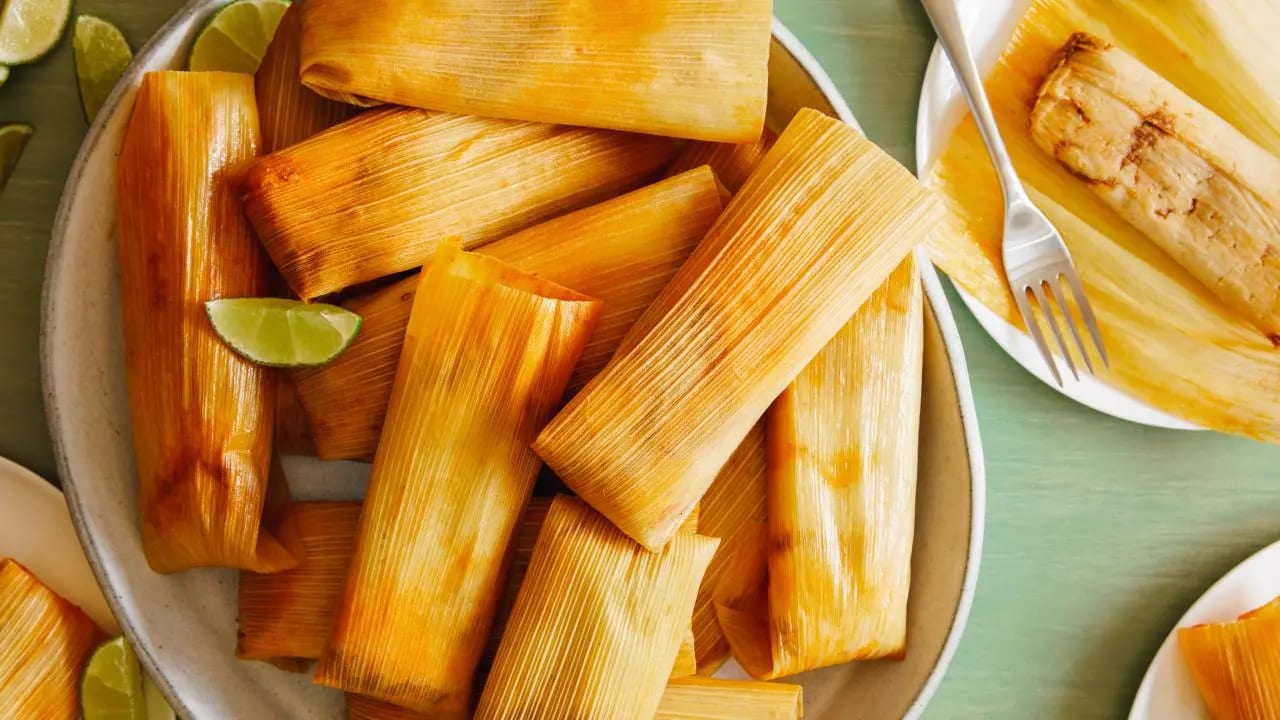 Tamales in corn husks on a plate with a lime wedge